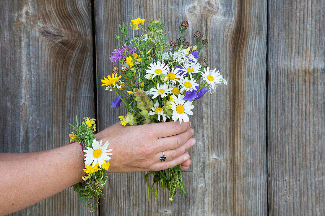 Wiesenblumenstrauß in Händen vor Holzwand