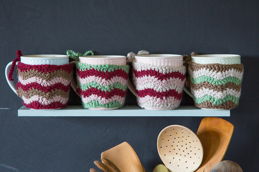 Mugs with knitted covers on a shelf in the kitchen