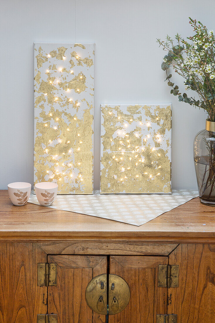 Canvas picture with golden accents and fairy lights on an antique wooden chest of drawers