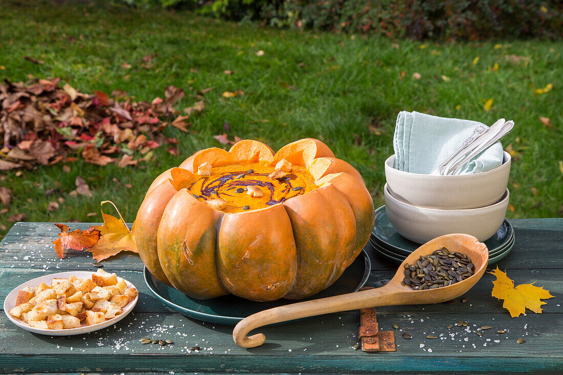 Kürbissuppe serviert in einem ausgehöhlten Kürbis mit Herbstlaub Dekoration