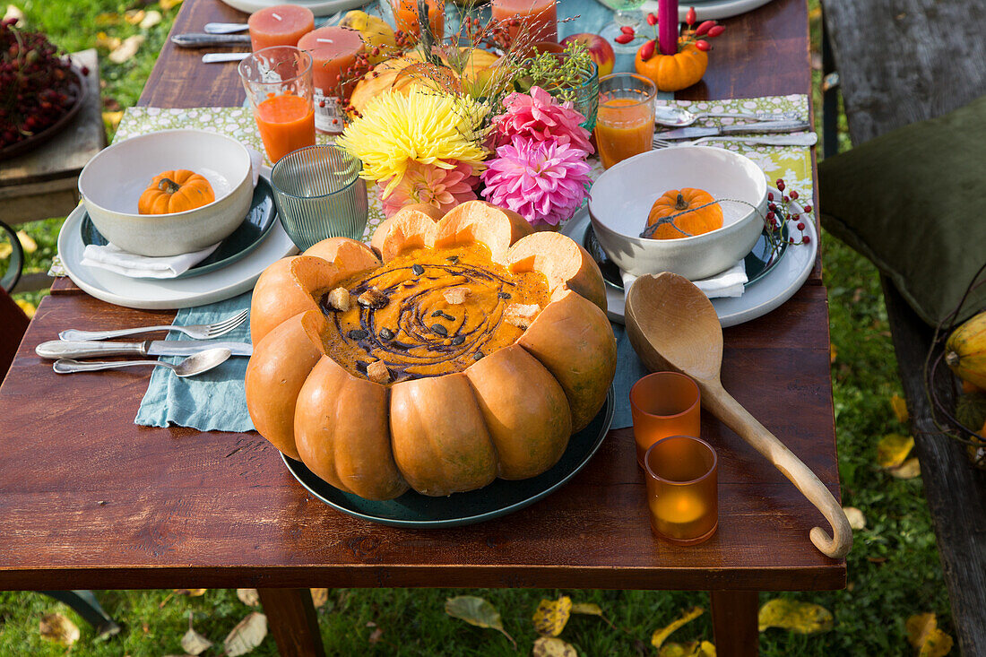 Herbstlich gedeckter Gartentisch mit Kürbissuppe im Kürbis und Blumendekoration