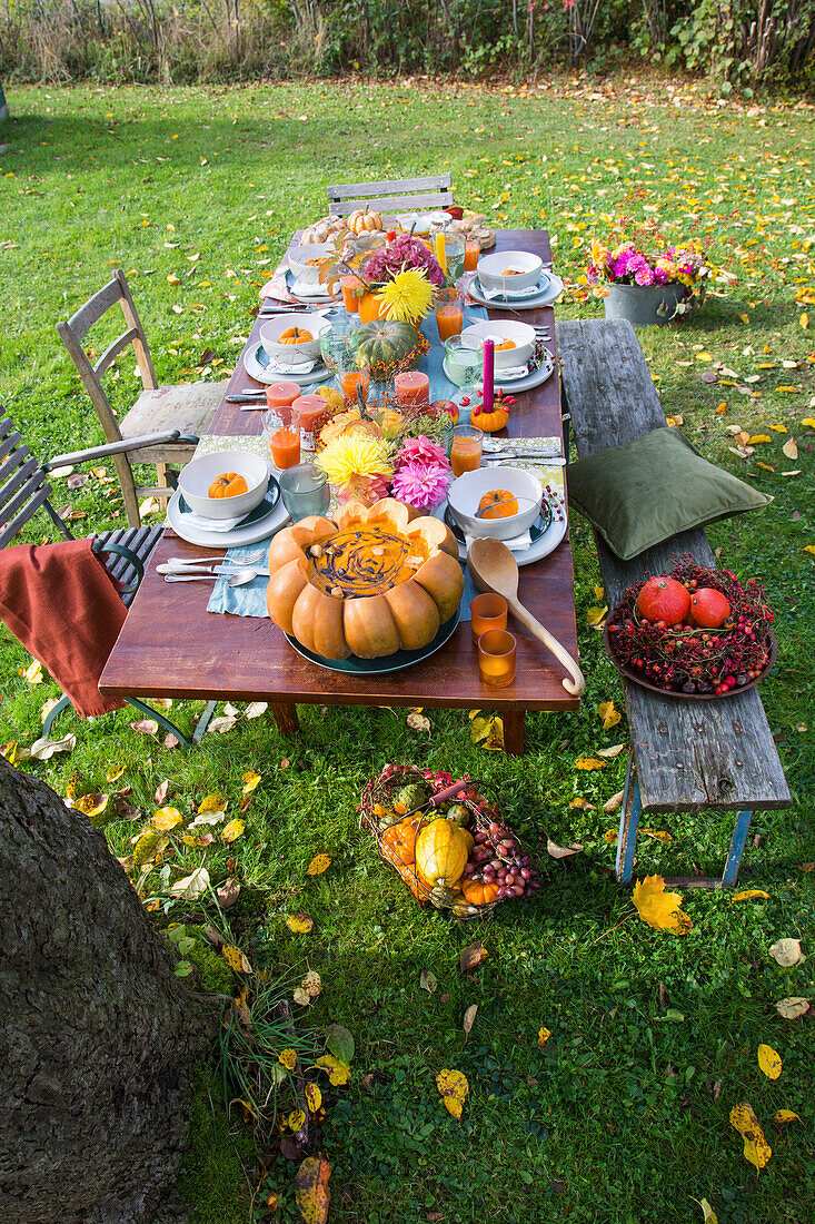 Herbstlich gedeckter Tisch im Garten mit Kürbisdeko und Blumenstrauß