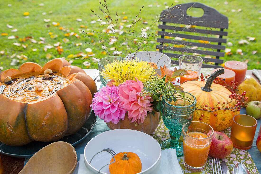 Herbstlich gedeckter Gartentisch mit Kürbissuppe und Blumenarrangement