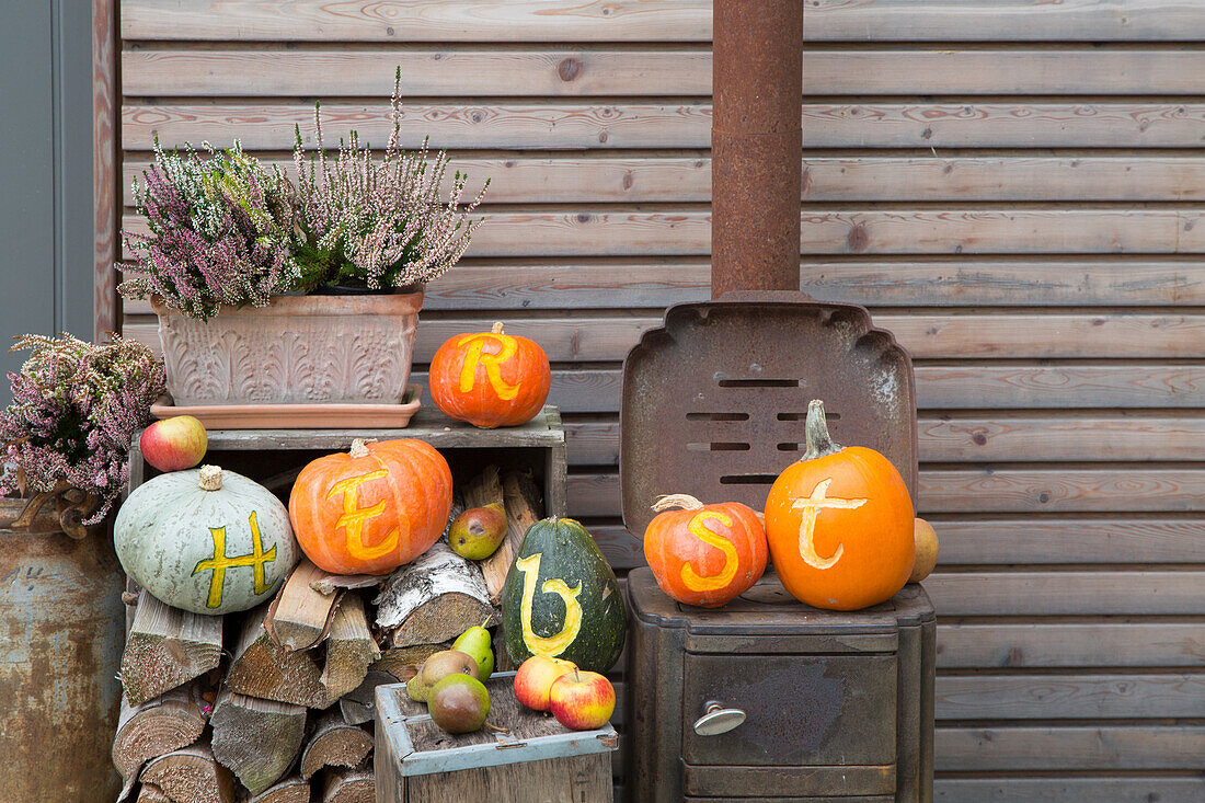 Herbstdeko mit beschrifteten Kürbissen und Brennholz vor Holzwand