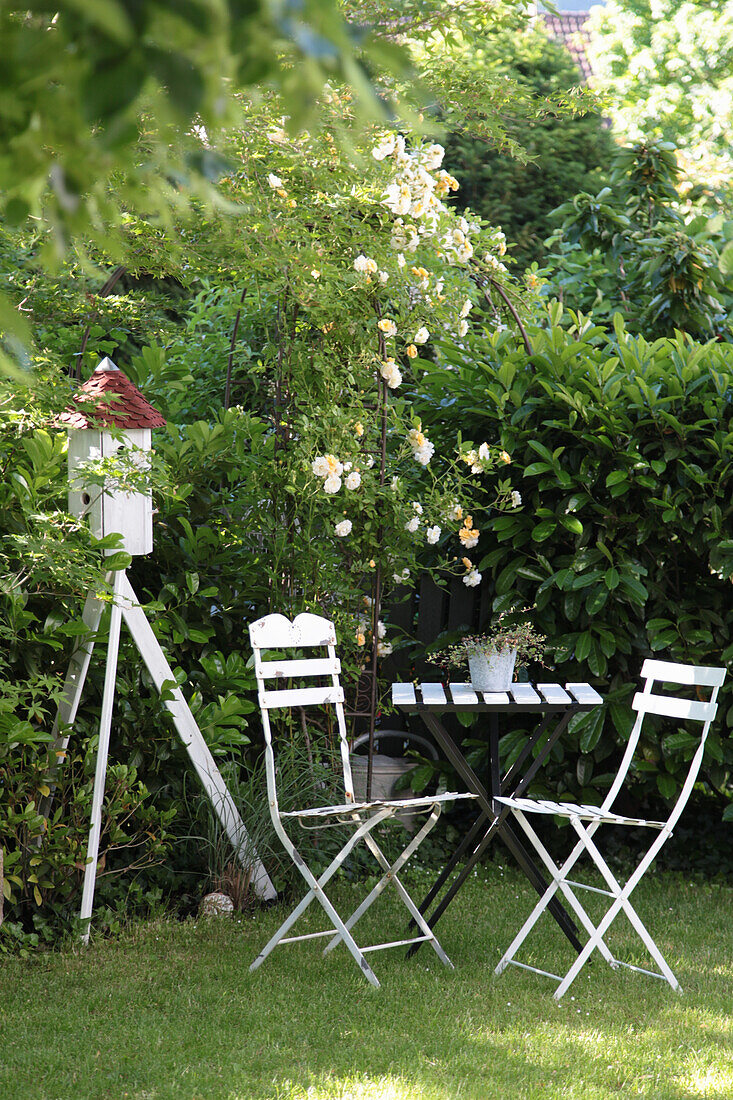 Table and chairs next to obelisk with climbing rose and dovecote