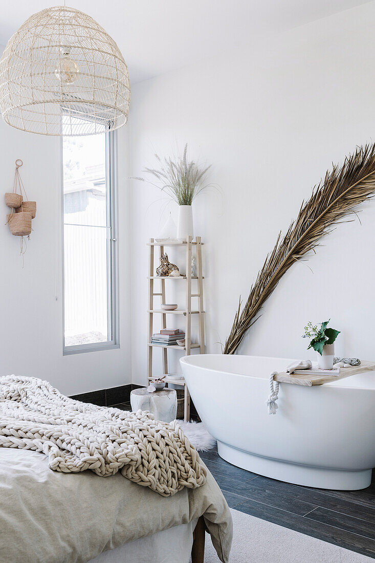 Palm frond behind free-standing bathtub in bedroom