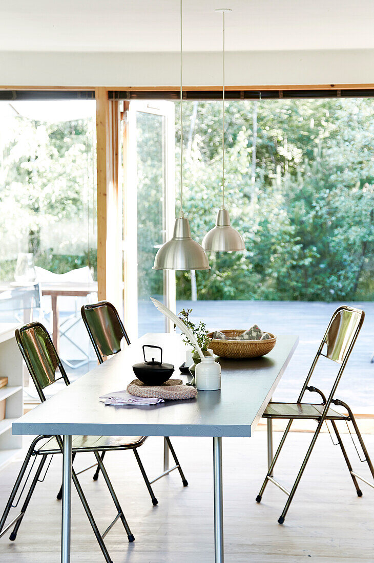 Dining table with folding chairs and pendant lights above and view of the terrace