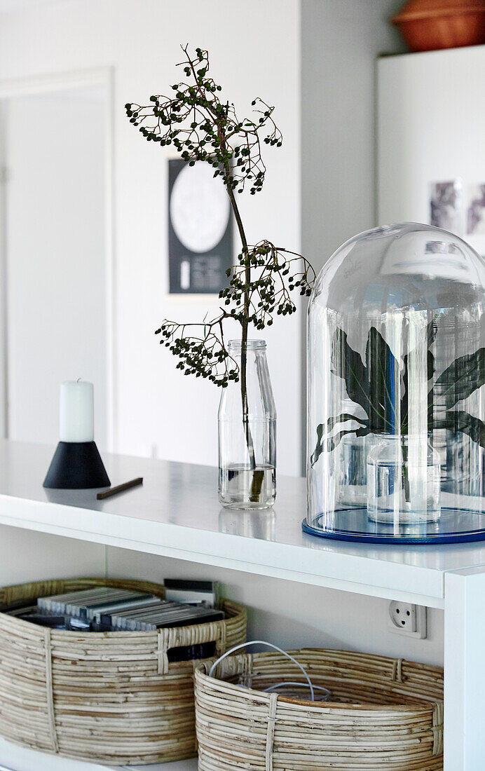 Baskets, candle, glass dome and glass bottle as a vase on a white shelf