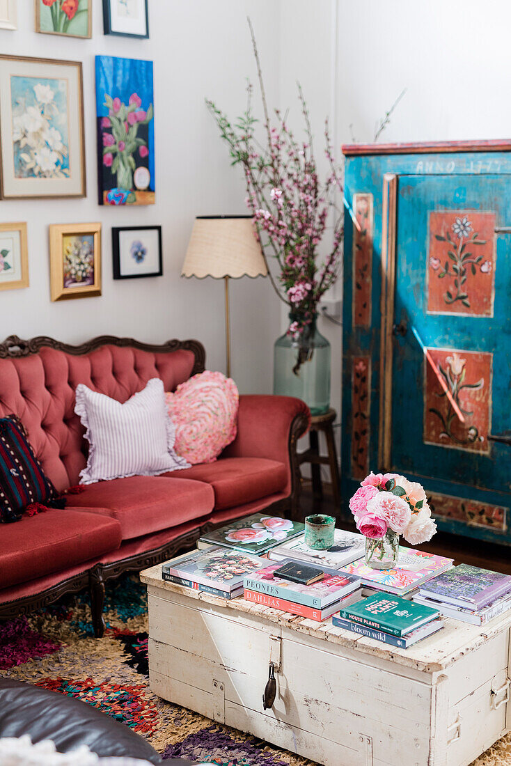 Sofa mit Kissen, darüber Bilder, bemalter Schrank und Holztruhe als Couchtisch im Wohnzimmer