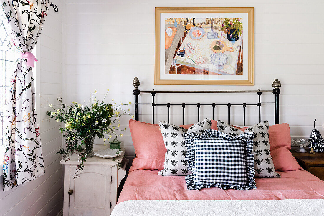Metalbett mit Kissen, daneben Nachtschränkchen mit Blumenstrauß in ländlichem Schlafzimmer
