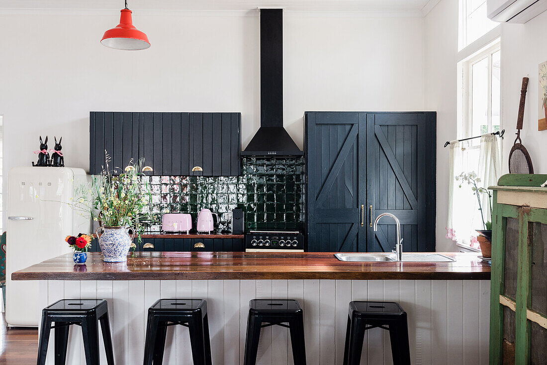 Kitchen counter with wooden top and classic bar stools, black cupboards and extractor hood