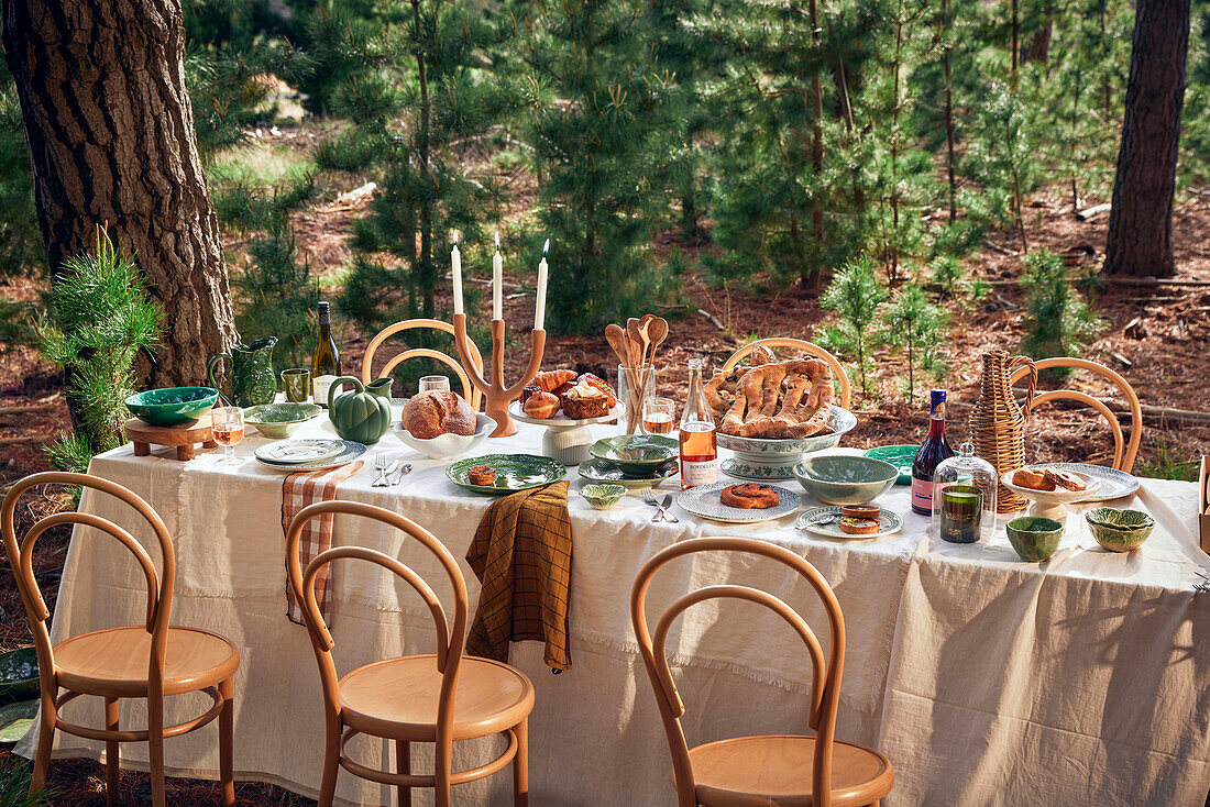 Festlich gedeckter Tisch mit Gebäck und Wein im Wald