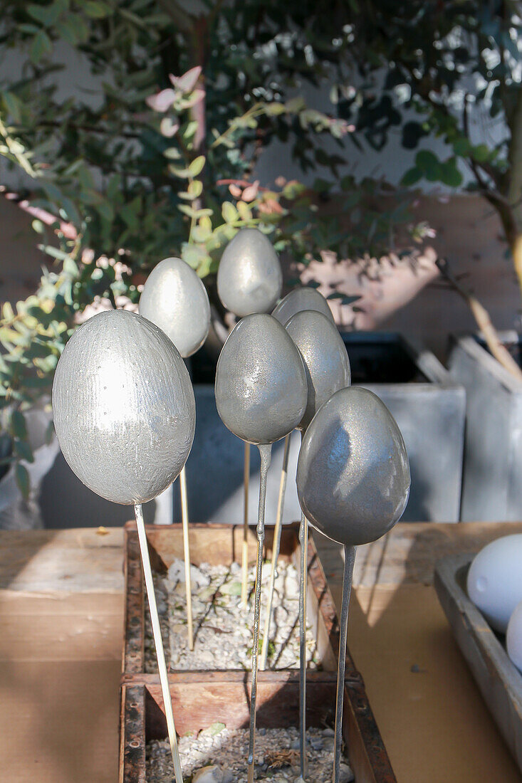 Silberne Dekoeier auf Holzstäben im Garten