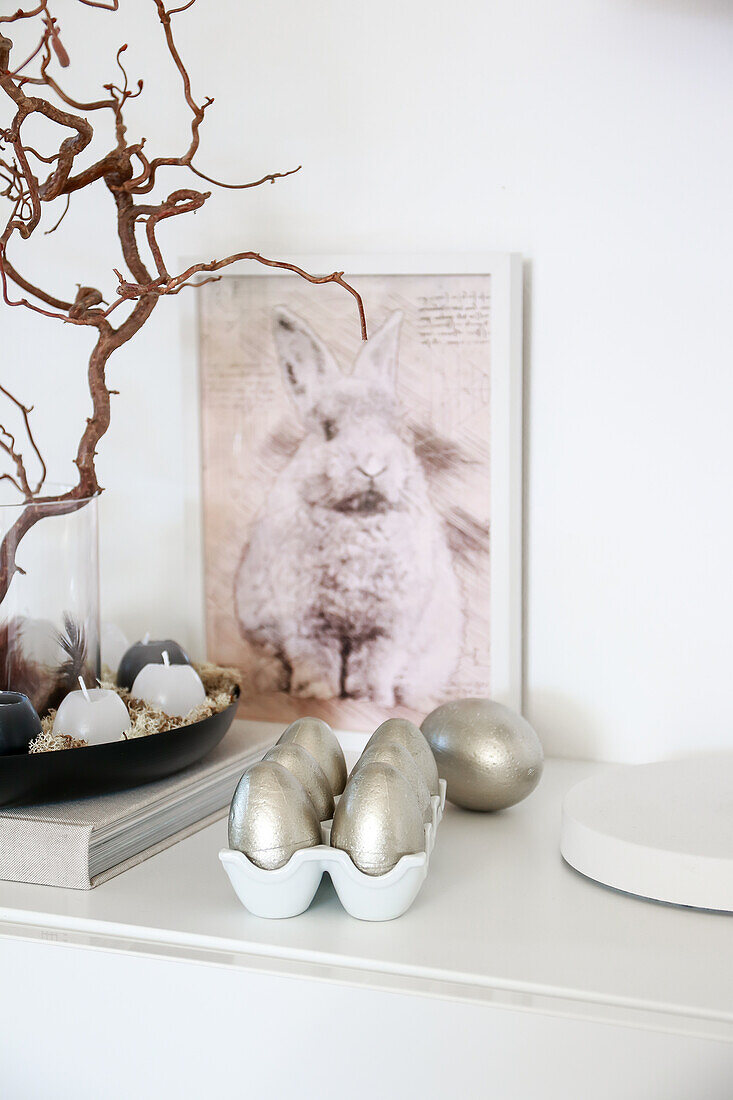 Hasenbild und silberner Eier auf weißem Sideboard