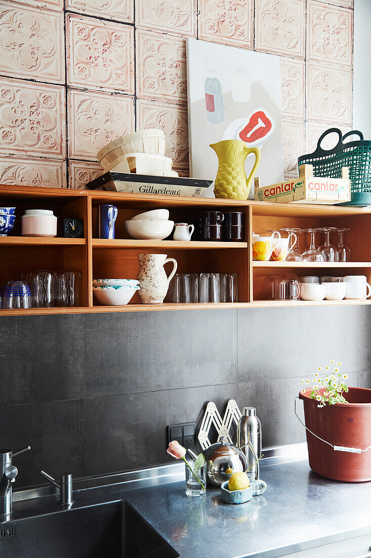 An open shelf with crockery in a kitchen with black tiles