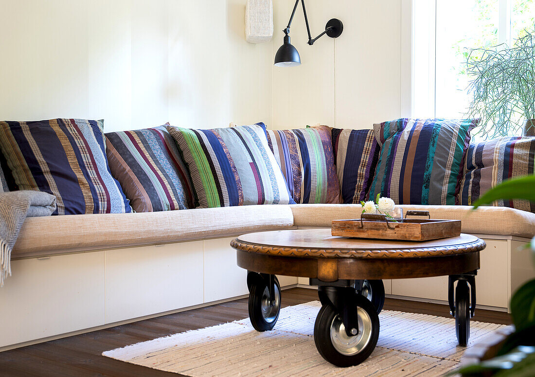 Corner sofa with colorful cushions and round coffee table on wheels