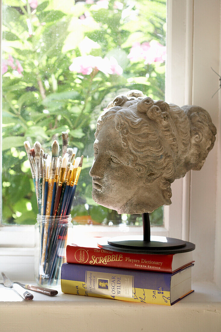 Bust of female head with books and paintbrushes on windowsill