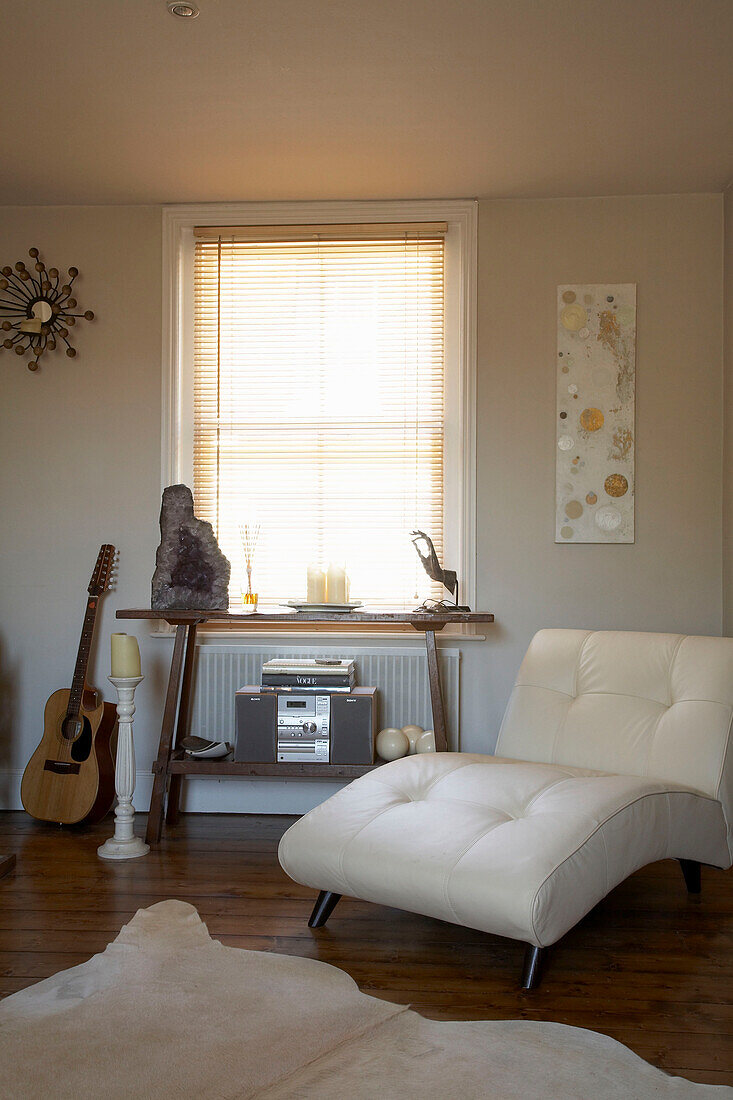 White leather armchair and guitar beside table below sunlit window with Venetian blinds
