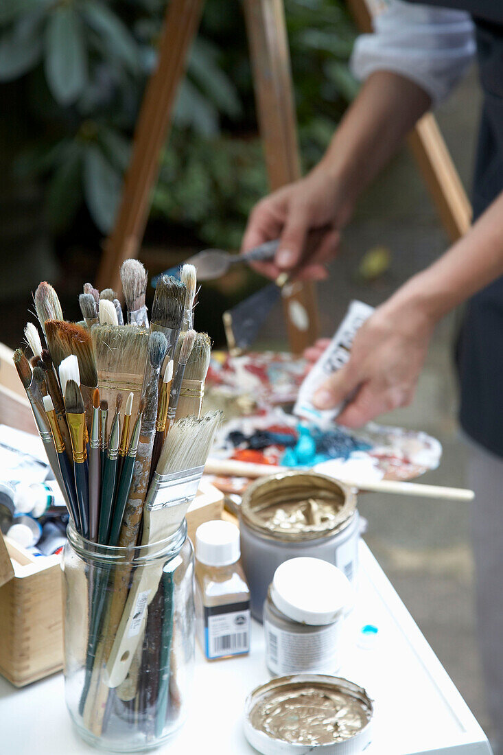 Artist mixing paints with paintbrushes on table
