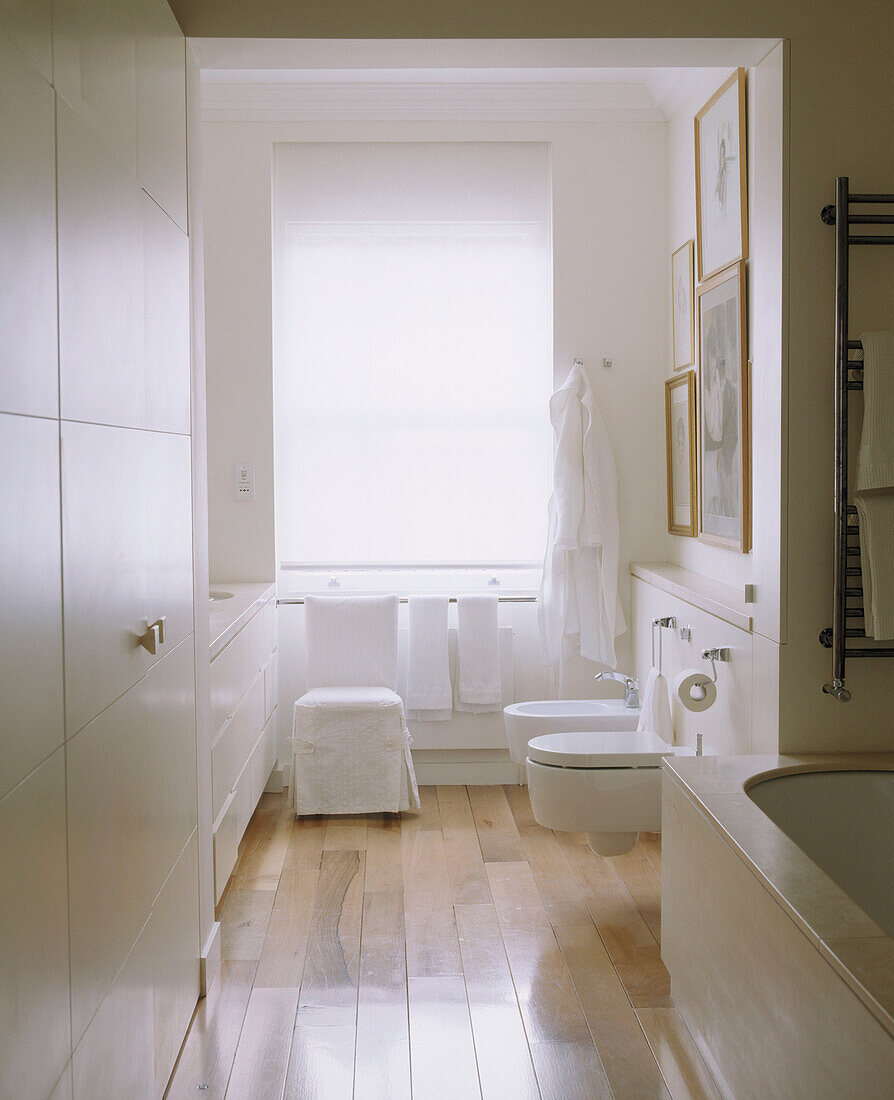 Ein modernes, in neutralen Farben gehaltenes Badezimmer mit wandmontierter Toilette und Bidet, Einbauschränken und Holzboden