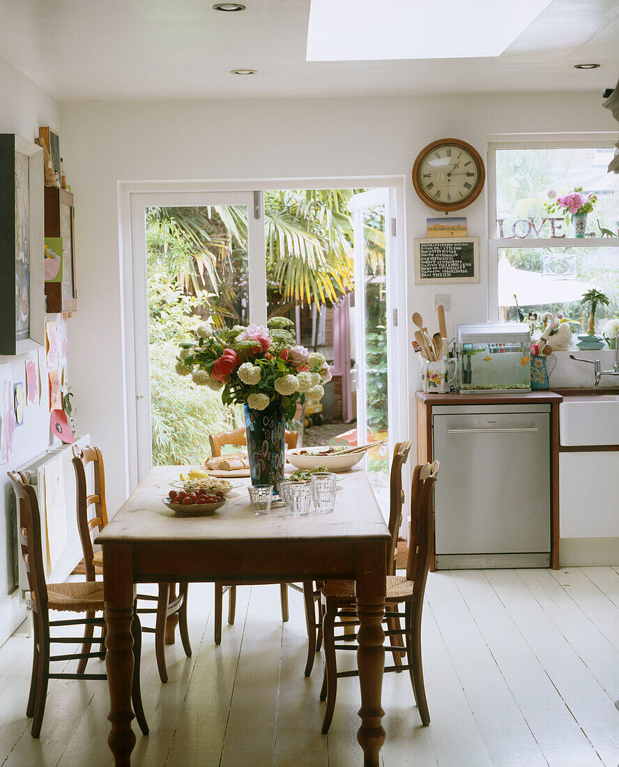 Ein traditioneller Essbereich an einer Seite einer Küche mit einem Tisch und Stühlen, einer Blumenvase und einer Uhr über einem Geschirrspüler aus Edelstahl