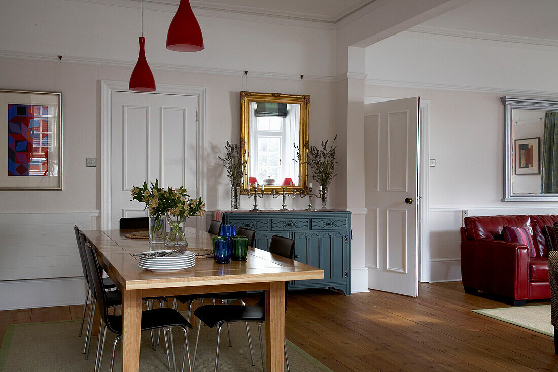 Wooden dining table with red pendant lights and painted sideboard in Devon home