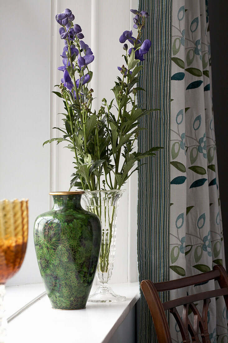 Vase und Schnittblumen (Delphinium) auf der Fensterbank eines Wohnzimmers in Devon