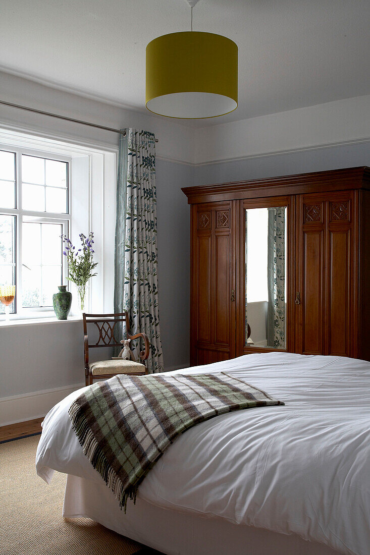 Holzkleiderschrank im Schlafzimmer in Devon mit karierter Decke auf dem Bett