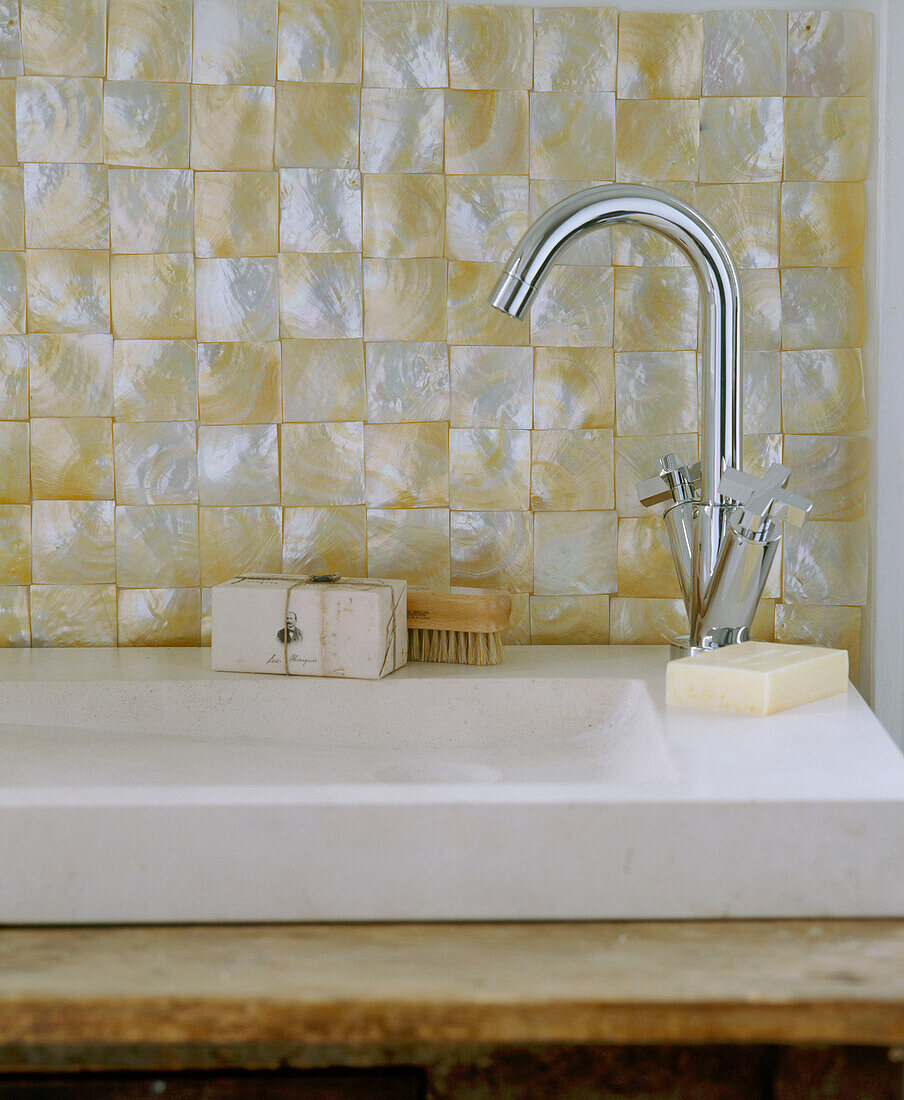 Detail eines modernen Badezimmers mit einem Steinwaschbecken mit verchromtem Wasserhahn und perlmuttfarbenen Fliesen