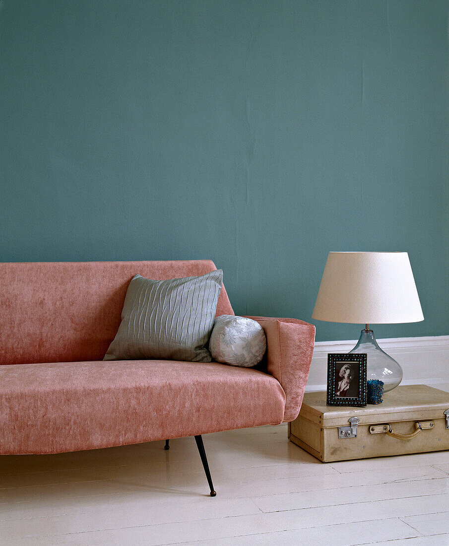 Pink sofa in green painted room next to table lamp on suitcase
