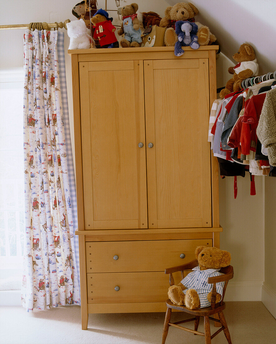 Detail of a traditional pine wardrobe in a children's bedroom with an exposed clothes rack and a novelty curtains