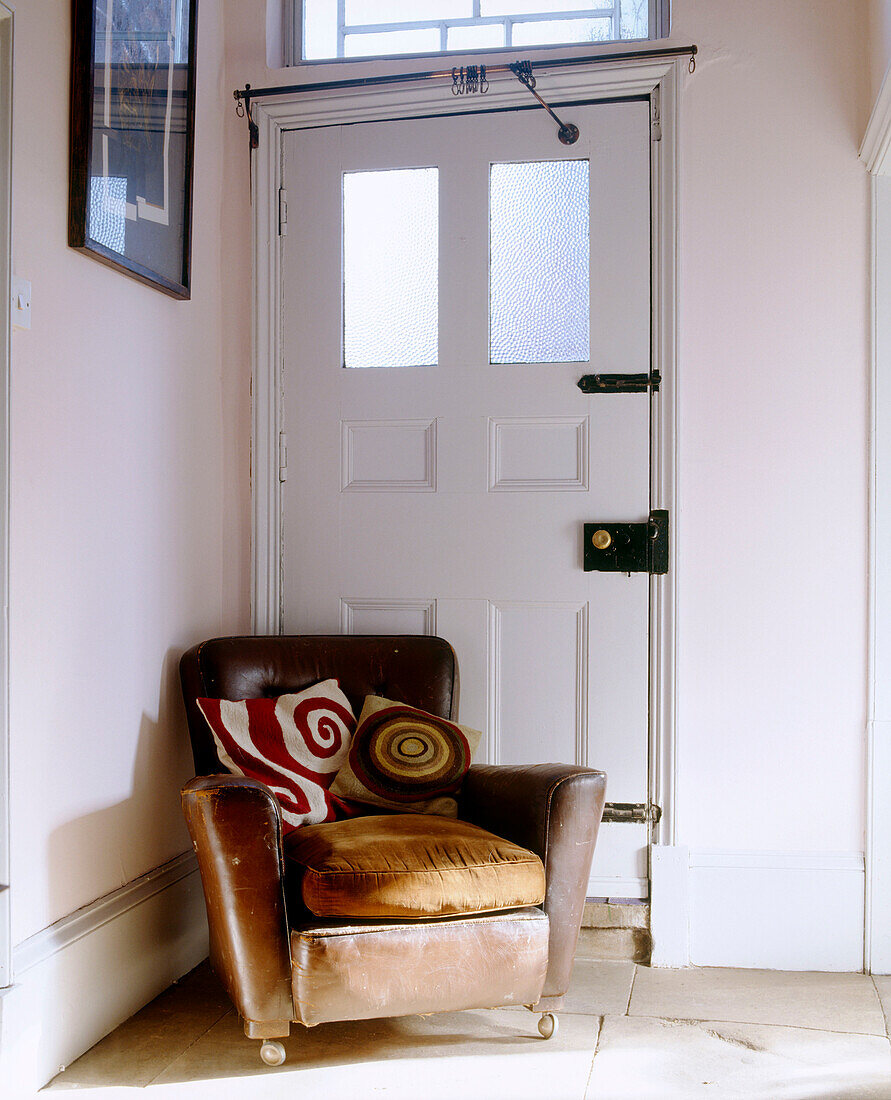 Alter Sessel mit Lederbezug und Kissen in Raumecke mit weißen Wänden und Fliesenboden
