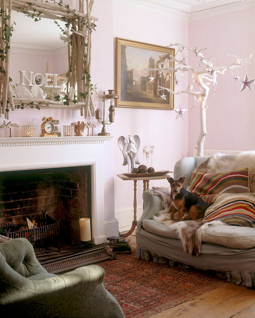 A traditional living room with a fireplace underneath an elaborately decorated mirror and with a dog on the sofa next to it