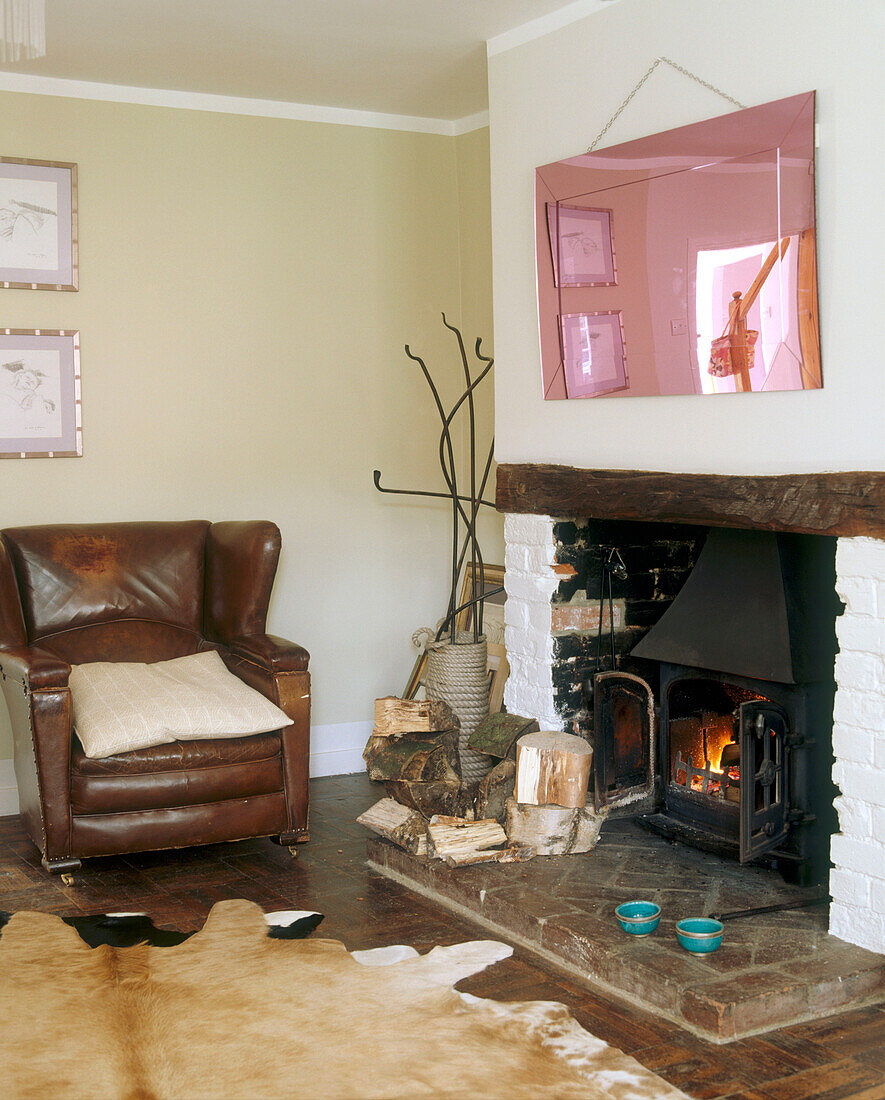 Ein traditionelles Wohnzimmer mit einem rosafarbenen Spiegel über einem offenen Kamin, umgeben von Holzscheiten und einem Ledersessel neben einem Tierfellteppich