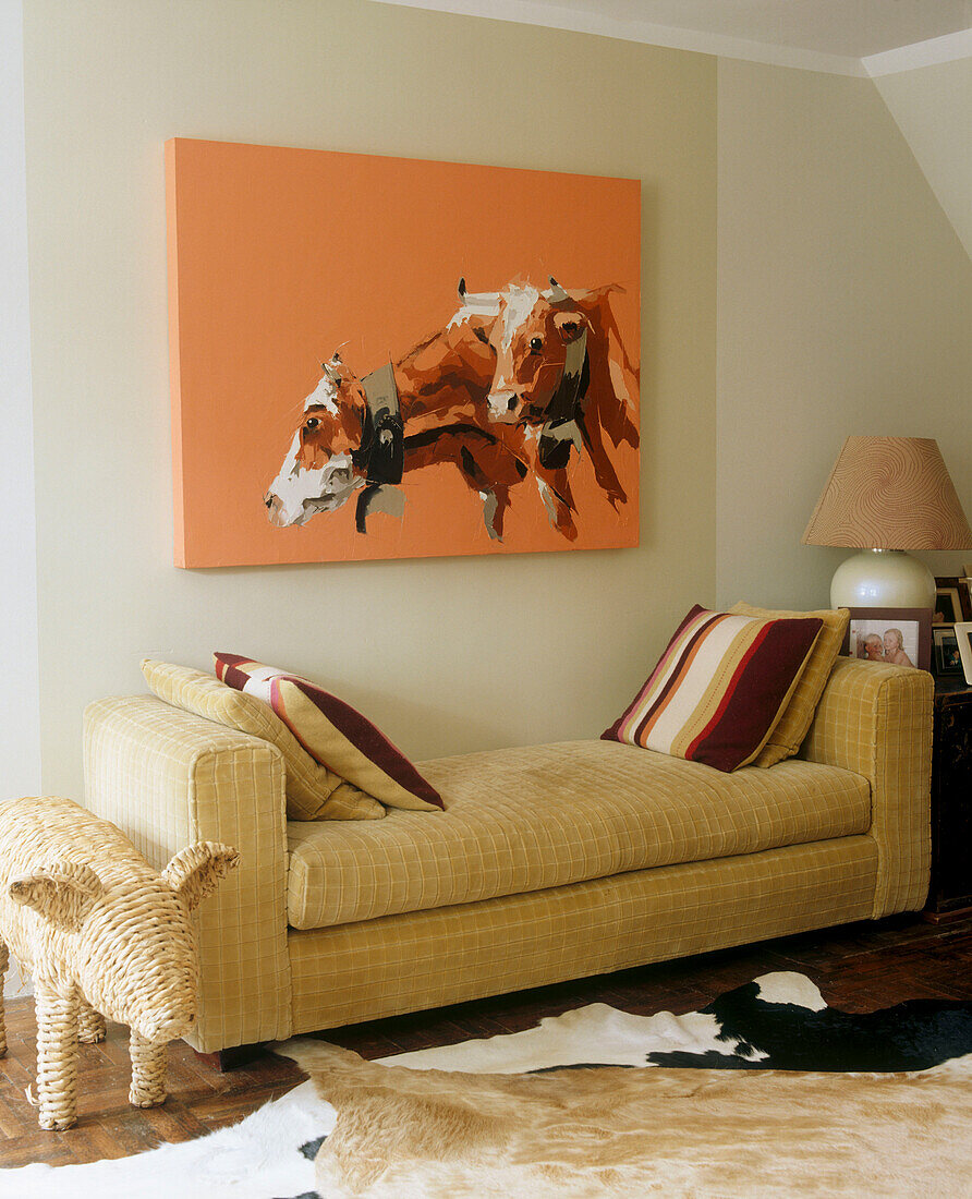 Modern living room detail of canvas painting of two cows backless sofa with cushions in front of an animal skin rug