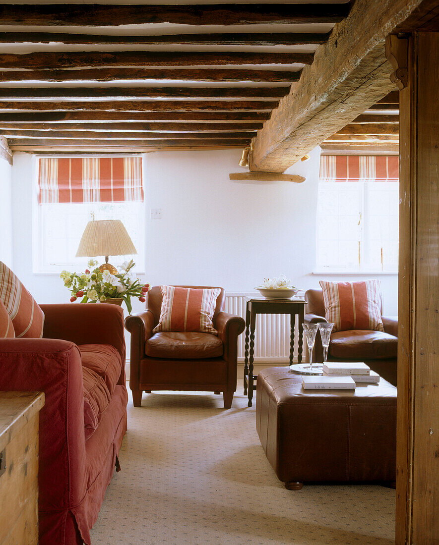 Traditionelles Wohnzimmer eines Landhauses mit freiliegenden Holzbalken über Leder-Couchtisch und rotem Sofa