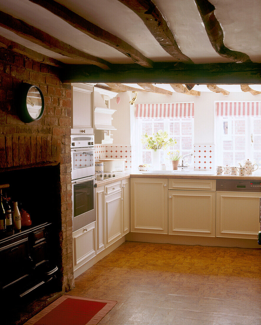 A traditional country kitchen with large wooden beams above a traditional stove surrounded by bare brick walls and a tiled floor