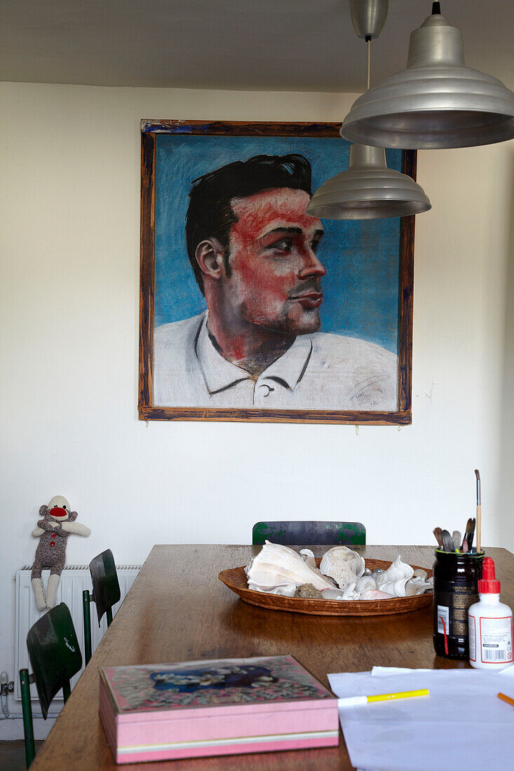 Männerportrait in einem Esszimmer mit Lampenschirmen aus Metall und Künstlerutensilien auf Tisch