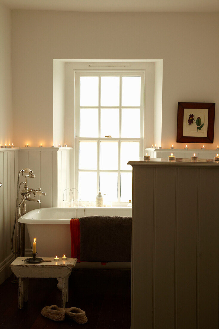 Rolltop-Badewanne mit Second-Hand-Tisch und brennenden Kerzen unter dem Fenster