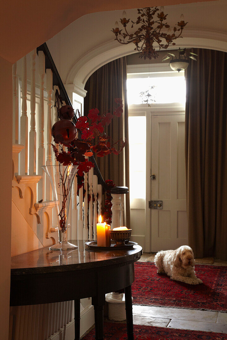 Lit candle on demilune console in hallway with pet dog and door curtains