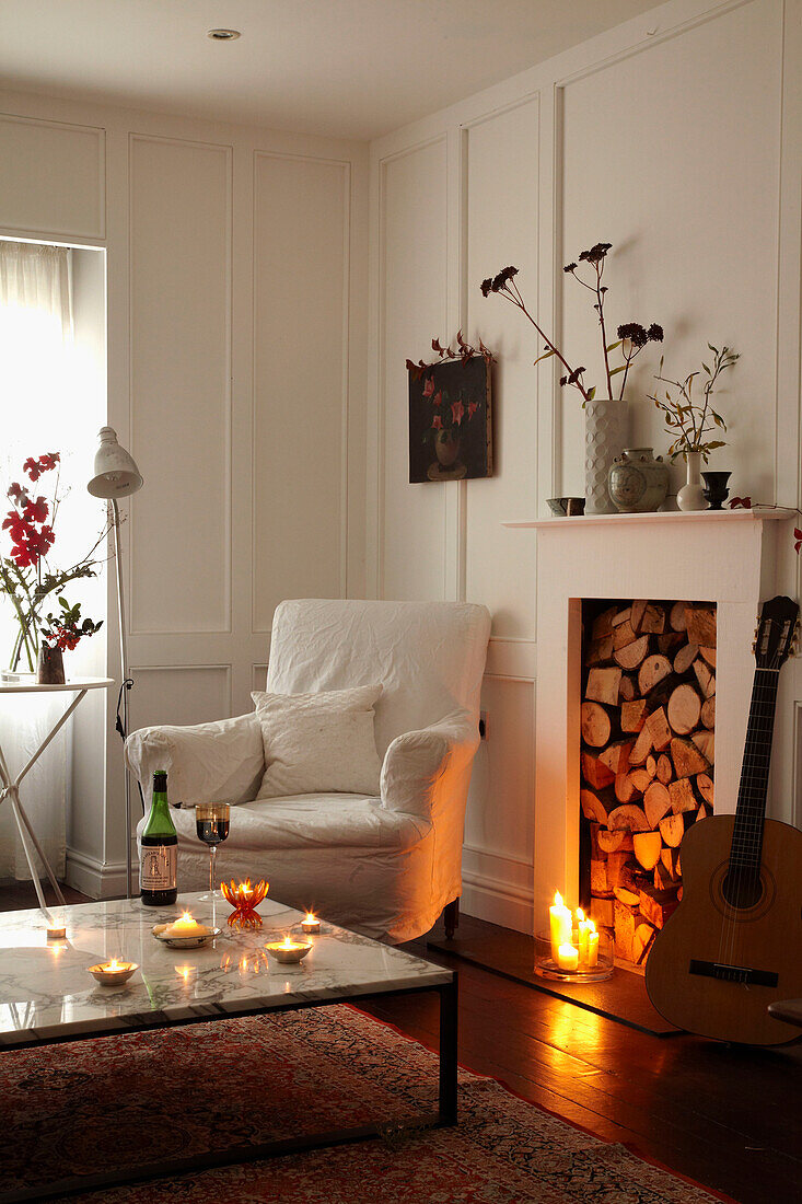 Gitarre am Kamin mit brennender Kerze in Zimmer mit weißem Sessel