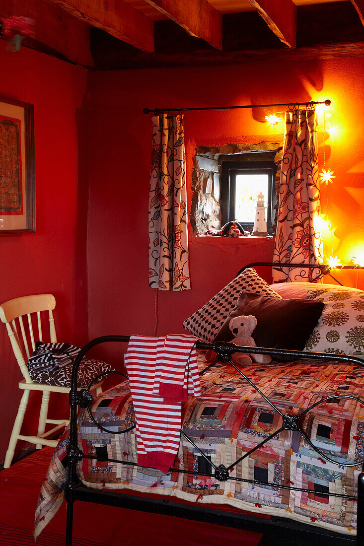 Patchwork quilt on metal framed bed in red beamed bedroom