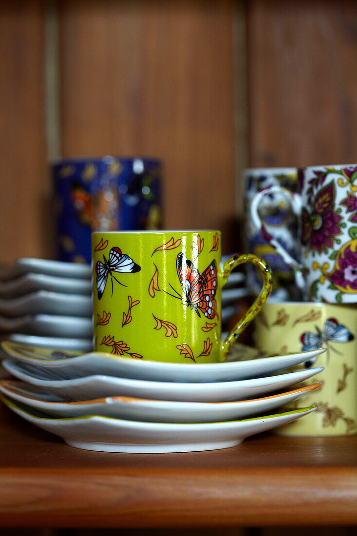 Variety of hand painted cups and saucers on wooden shelf