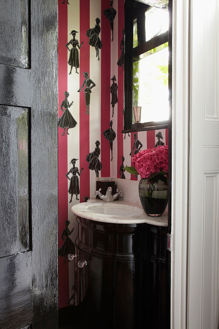 Marmorwaschbecken und Figuren auf rosa gestreifter Tapete in der Gästetoilette eines Londoner Hauses