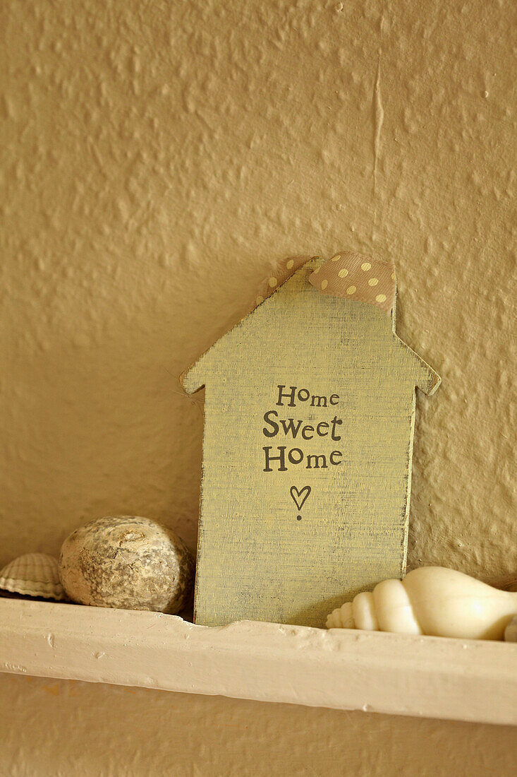 Muscheln und Dekohaus mit der Aufschrift 'Home Sweet Home' auf Regal in Haus in West Sussex, England, UK