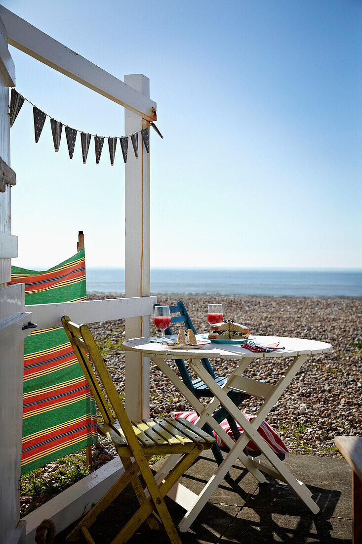 Tisch und Stühle auf der Terrasse einer Strandhütte am Kieselstrand an der Küste von West Sussex, England, UK