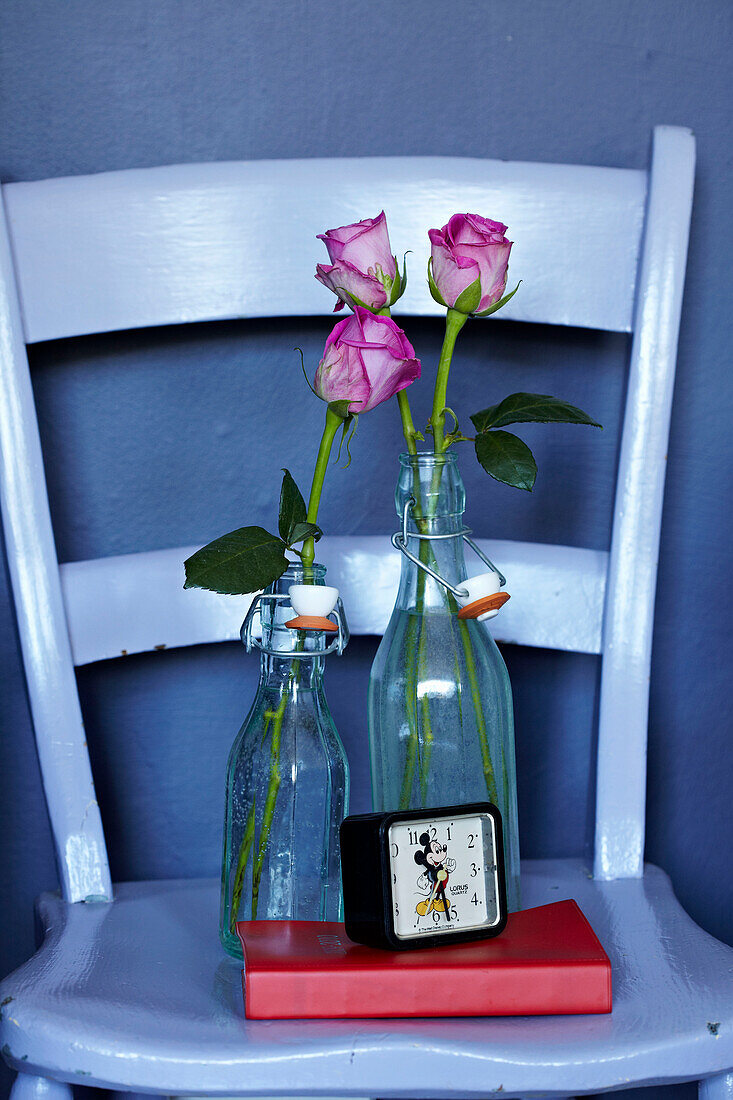 Cut roses in vintage bottles on blue painted chair Brighton Sussex, England, UK