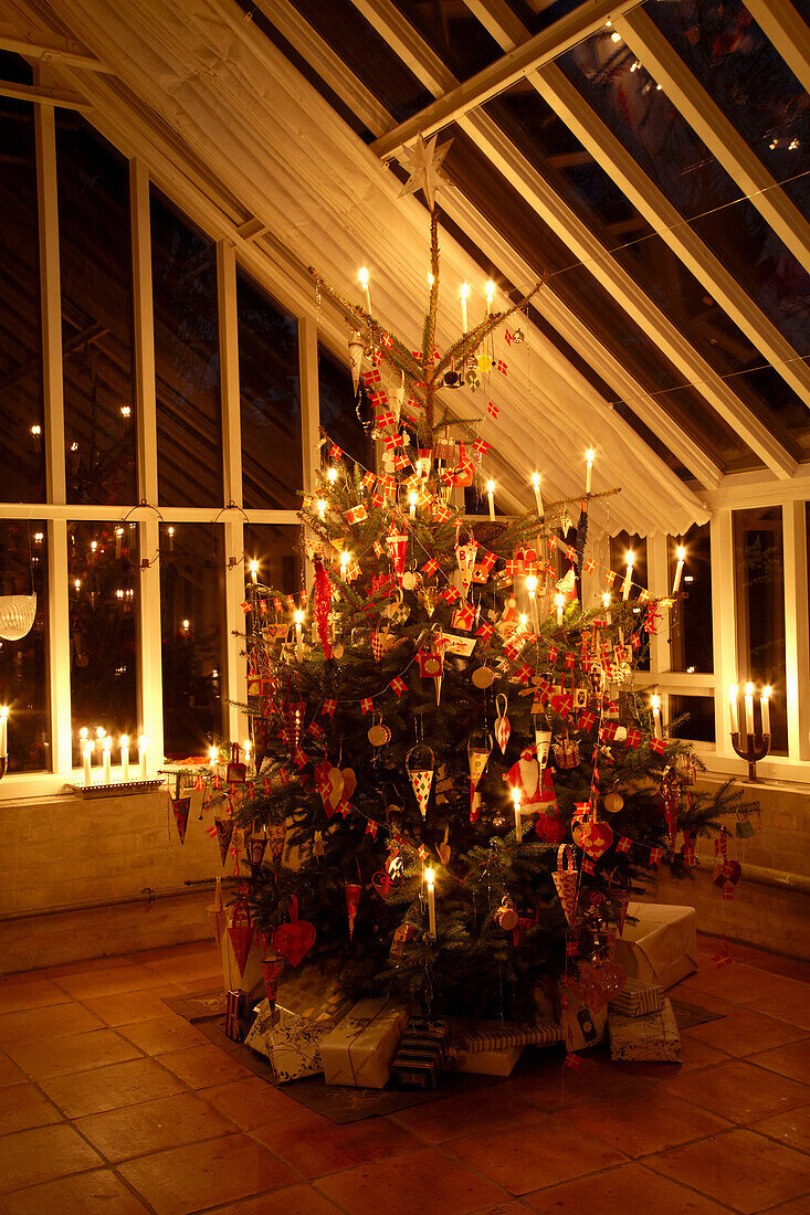 Beleuchteter Weihnachtsbaum mit eingepackten Geschenken in Wintergarten mit hohen Decken