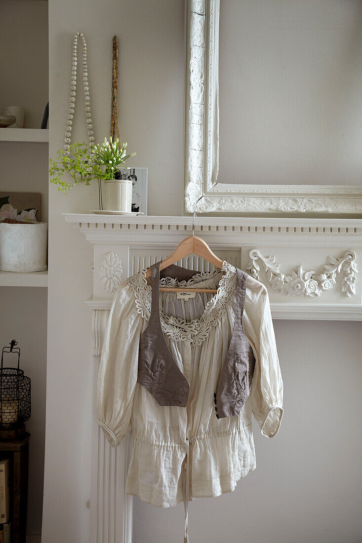 Lace blouse and waistcoat hang on fireplace of London home