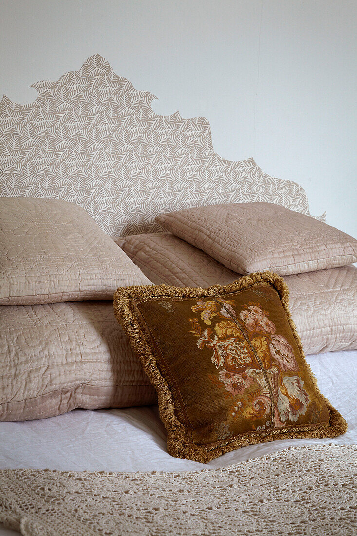 Goldfarbenes Kissen und mehrere gesteppte Kissen auf Bett eines Londoner Hauses